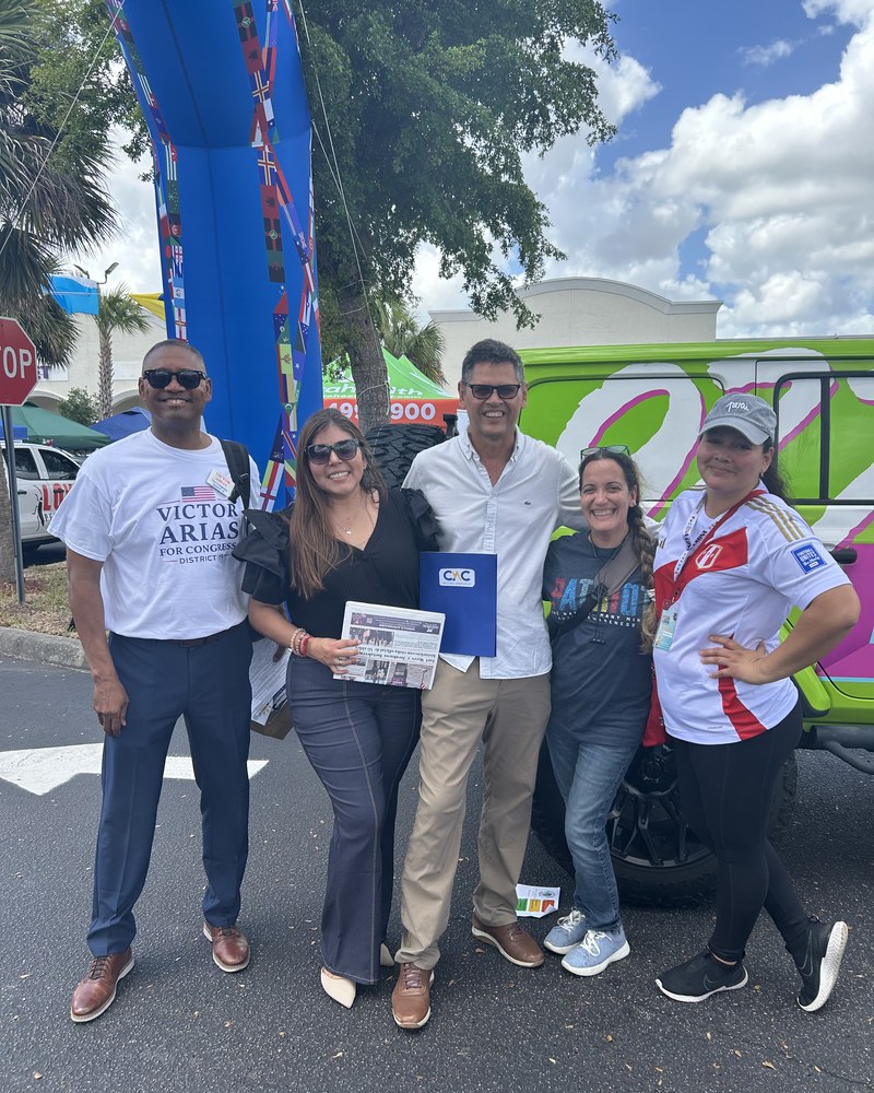 Five adults pose together outdoors beside a brightly colored vehicle.
