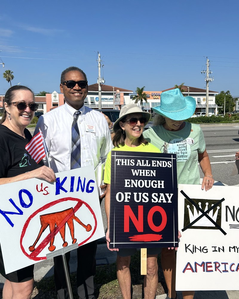 Victor Arias stands outdoors with three community members holding handmade signs.