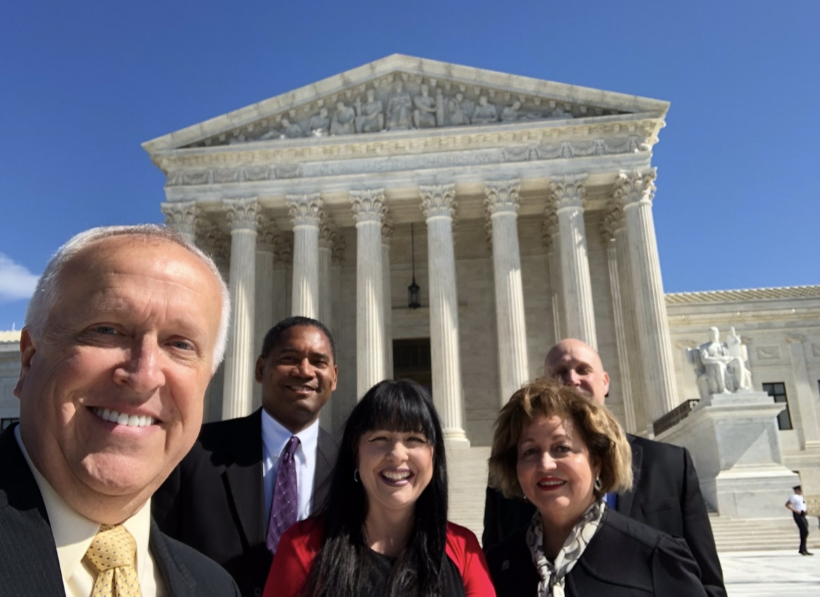 Five adults take a group photo outside a columned government building.